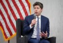 Sam Altman, CEO of OpenAI, sitting in front of American flag