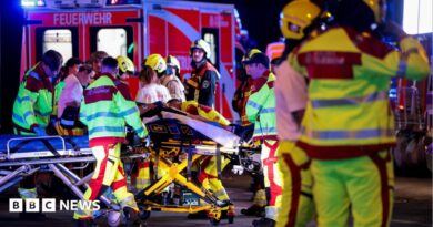 A number of emergency services personnel standing near an ambulance, with a person on a stretcher