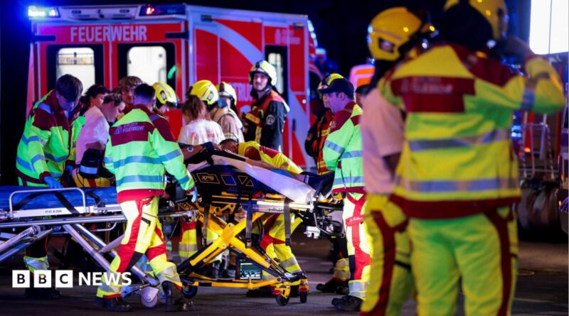 A number of emergency services personnel standing near an ambulance, with a person on a stretcher
