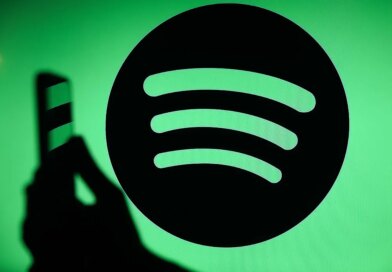 The Spotify logo displays on a screen with a person holding a phone.