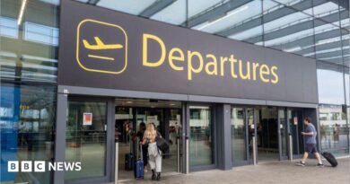 The departures entrance at Gatwick Airport with large yellow "Departures" signage above glass doors. Travellers with luggage can be seen entering the terminal building.