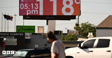 Man walks through road and looks up at sign that says 118 degrees and 05:15 pm