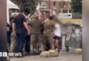 A group of men in army uniforms carrying a man into a van