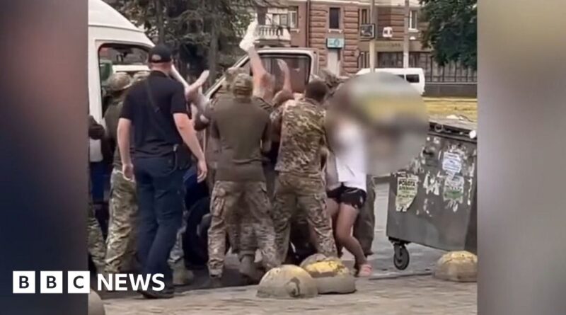 A group of men in army uniforms carrying a man into a van