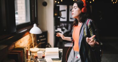 Young Latinx woman sitting at the desk in her Los Angeles apartment, receiving happy news over the social networks or just having a nice day, dancing to the music.