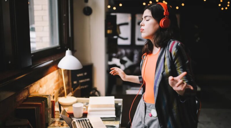 Young Latinx woman sitting at the desk in her Los Angeles apartment, receiving happy news over the social networks or just having a nice day, dancing to the music.
