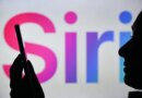 An image of a woman holding a cell phone in front of the Siri logo displayed on a computer screen.