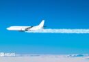 A jet plane flies across the blue sky, with white contrails coming from its engines