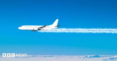 A jet plane flies across the blue sky, with white contrails coming from its engines