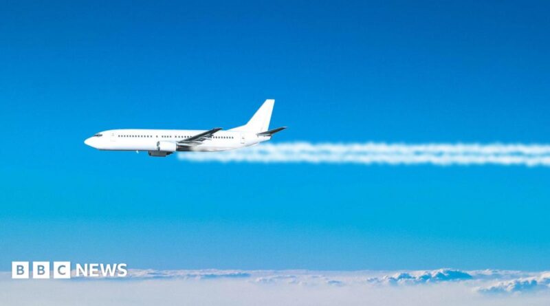 A jet plane flies across the blue sky, with white contrails coming from its engines