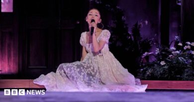 Ariana Grande sits on the stage, surrounded by flowers, as she sings on her Eternal Sunshine tour