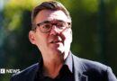 Andy Burnham wearing a dark suit and glasses.