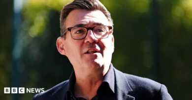 Andy Burnham wearing a dark suit and glasses.