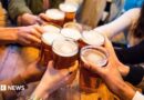 A young group of friends clinking pint glasses of beer together around a pub table