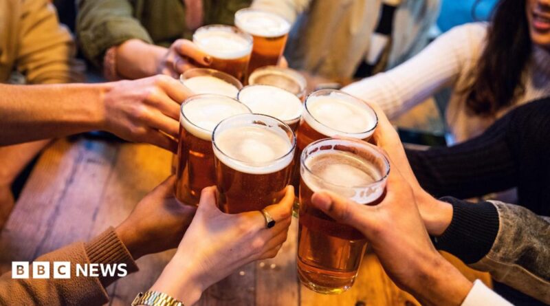 A young group of friends clinking pint glasses of beer together around a pub table