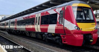 A red and white train is parked on railway tracks next to a train station.