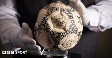 A person wearing white gloves places the football used in the 1986 World Cup quarter-final on a stand