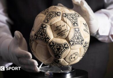 A person wearing white gloves places the football used in the 1986 World Cup quarter-final on a stand