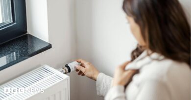 Partial side view of a woman who is holding her jumper close around her neck with one hand and turning up her radiator with the other