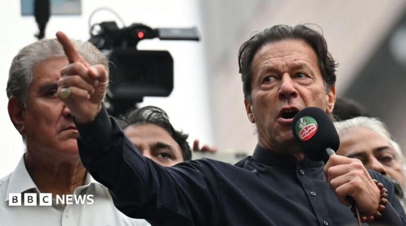 Imran Khan wearing a black button-up shirt and speaking into a microphone, points dramatically. Behind him are other men, and a television camera