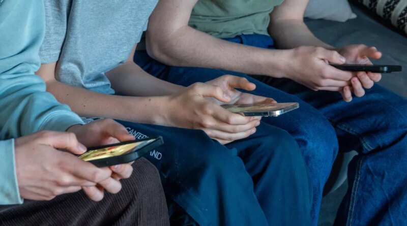Three teenage boys look at their smartphone screens.