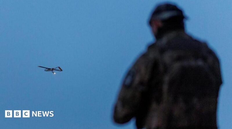 A Ukrainian soldier operating a drone, which is flying in the air in the background