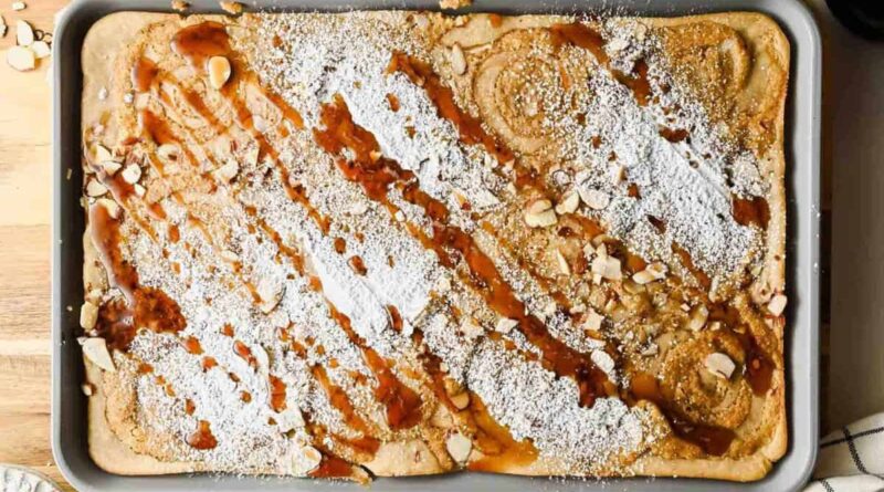 Baked sheet pan almond croissant pancakes dusted with powdered sugar and drizzled with maple syrup.
