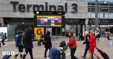 Passengers push luggage outside Terminal 3 as a gate information screen can be seen in the background