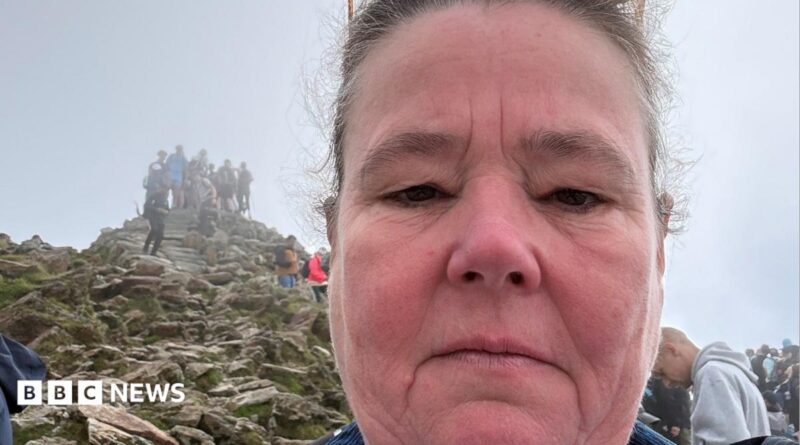 Helen has a neutral expression as she takes a selfie overlooking the summit of Yr Wyddfa