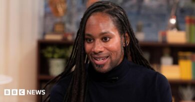 Jason Arday pictured during a TV interview in March 2023. He wears a black turtle-neck top.