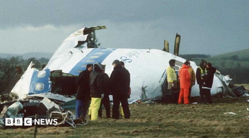 Emergency service workers stand next to the wreckage of Pan Am flight 103 in a field east of Lockerbie.