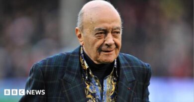Al Fayed is wearing a suit jacket as he walks across a football pitch