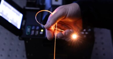 A hand holds a single strand of fiber in a darkened room, with light pouring from its tip.