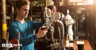 A man wearing a blue top pouring a pint in a pub