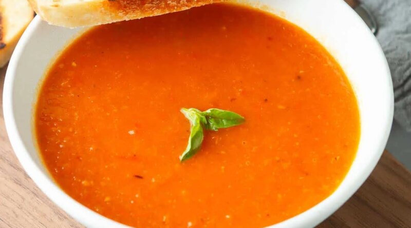 A bowl of tomato soup and a slice of grilled bread.