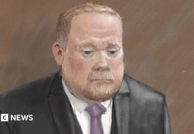 Courtroom sketch of Robert Bush in a dark three-piece suit standing alone against a plain brown background. He wears a light-coloured shirt and a purple tie. The illustration is rendered in soft pencil and pastel tones.
