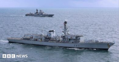 A grey Royal Navy warship is in the foreground with a grey Russian vessel in water in the background