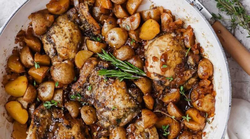 Apple cider chicken thighs nestled with baby potatoes and onion in a glossy skillet sauce.