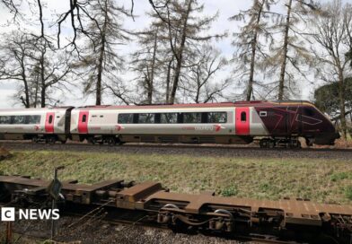 The cab and first carriage of a CrossCountry train travels on tracks in the countryside. In the background trees and fields can be seen.