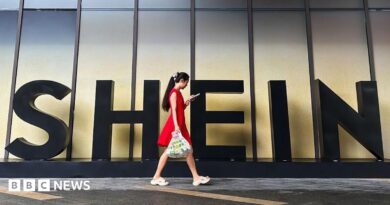 A woman in a red dress looks at her smartphone while walking past a Shein sign outside the company's office in Guangzhou, China. 