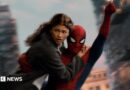Spider-Man swings through the city on web whilst holding MJ, played by Zendaya.