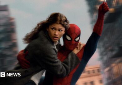 Spider-Man swings through the city on web whilst holding MJ, played by Zendaya.