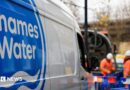 A shot of a Thames Water van. In the background there are two men wearing hi-vis clothing and hard hats and standing in an area that is boarded off by blue fences. 