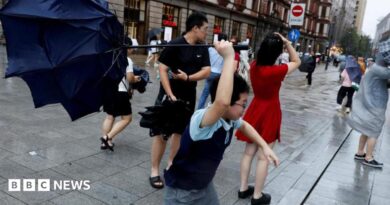 People holding umbrellas along a street in Shanghai. One boy is seen trying to hold on to an inverted umbrella as winds intensify