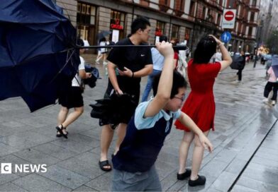 People holding umbrellas along a street in Shanghai. One boy is seen trying to hold on to an inverted umbrella as winds intensify