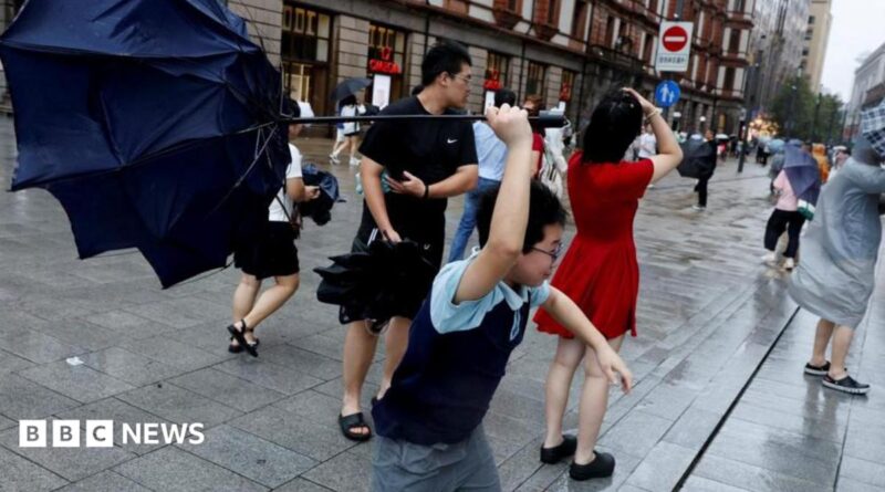 People holding umbrellas along a street in Shanghai. One boy is seen trying to hold on to an inverted umbrella as winds intensify