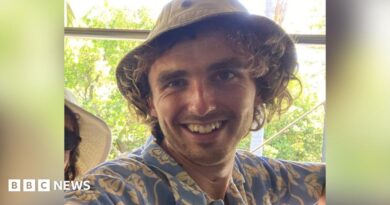 Finn Joughin, a 22-year-old student activist, was arrested in Umm Al-Kheir on Saturday. He is smiling and looking directly at the camera. He is wearing a soft canvas hat and wearing a blue shirt with cream-coloured floral motifs.