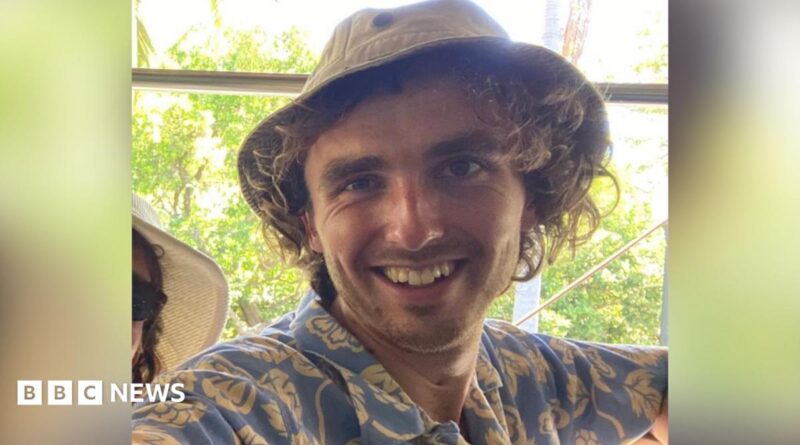 Finn Joughin, a 22-year-old student activist, was arrested in Umm Al-Kheir on Saturday. He is smiling and looking directly at the camera. He is wearing a soft canvas hat and wearing a blue shirt with cream-coloured floral motifs.