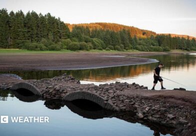 View of a depleted reservoir with a boy walking across a bridge with a fishing rod