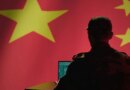 A man sits in front of a computer and the Chinese flag.